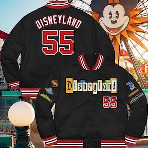 May include: Black baseball jacket with red and white stripes on the sleeves and collar. The jacket has a large "DISNEYLAND" text and the number "55" on the back. The front of the jacket has a smaller "DISNEYLAND" text and the number "55" on the bottom right side. The jacket has various Disney-themed patches on the sleeves.