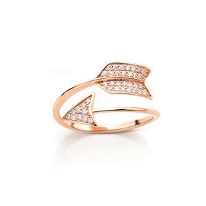 Könnte beinhalten: Ein Ring aus Roségold mit einem Doppelpfeil-Design. Der Pfeil ist mit klaren Zirkonia-Steinen besetzt.