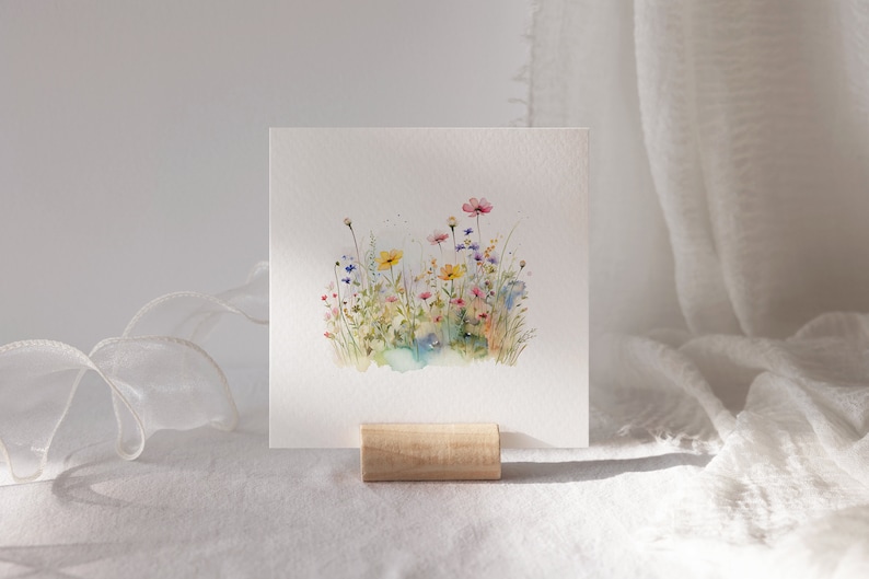 May include: A watercolor painting of a field of wildflowers in shades of pink, yellow, blue, and green. The flowers are arranged in a cluster, with some stems extending beyond the group. The painting is on a white background.