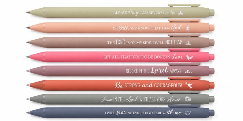 May include: A set of eight retractable ballpoint pens in various muted colors, each featuring a unique white printed religious quote and a small icon. The pens are arranged horizontally, displaying phrases like Always Pray, Be Still, and Trust in the Lord.
