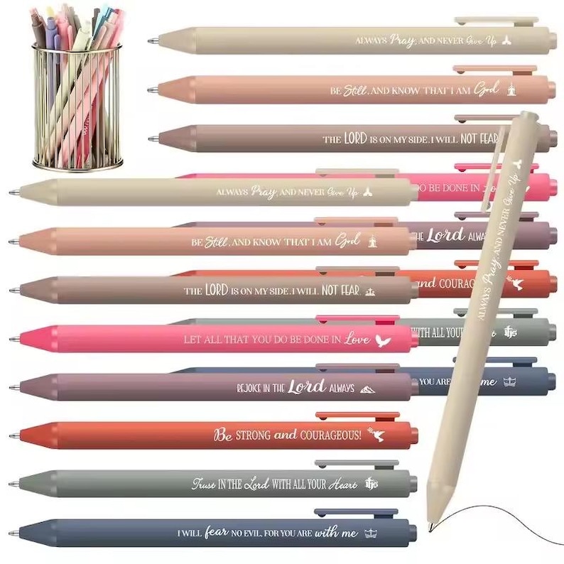 May include: A collection of retractable ballpoint pens in various muted colors, each featuring a unique religious quote printed in white. The pens are displayed individually and in a gold-toned wire mesh cup holder. Each pen includes a clip and a tip.