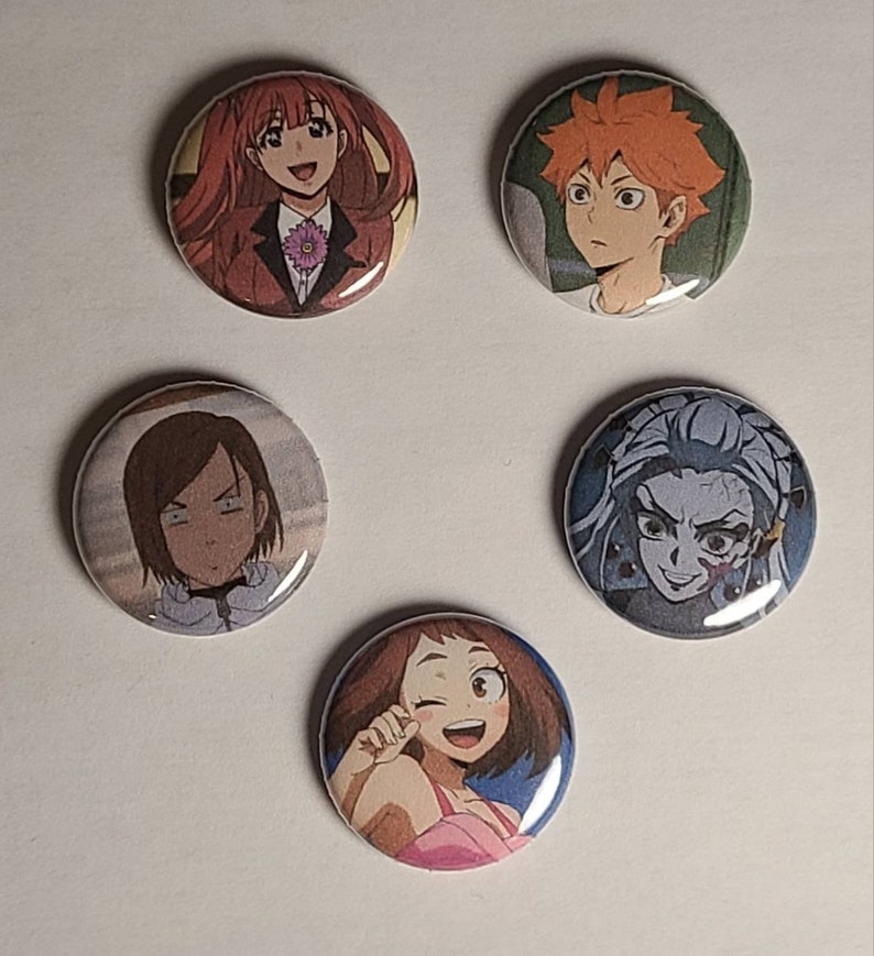 May include: Five round button pins featuring anime characters. The pins are colorful and feature different characters with various expressions.