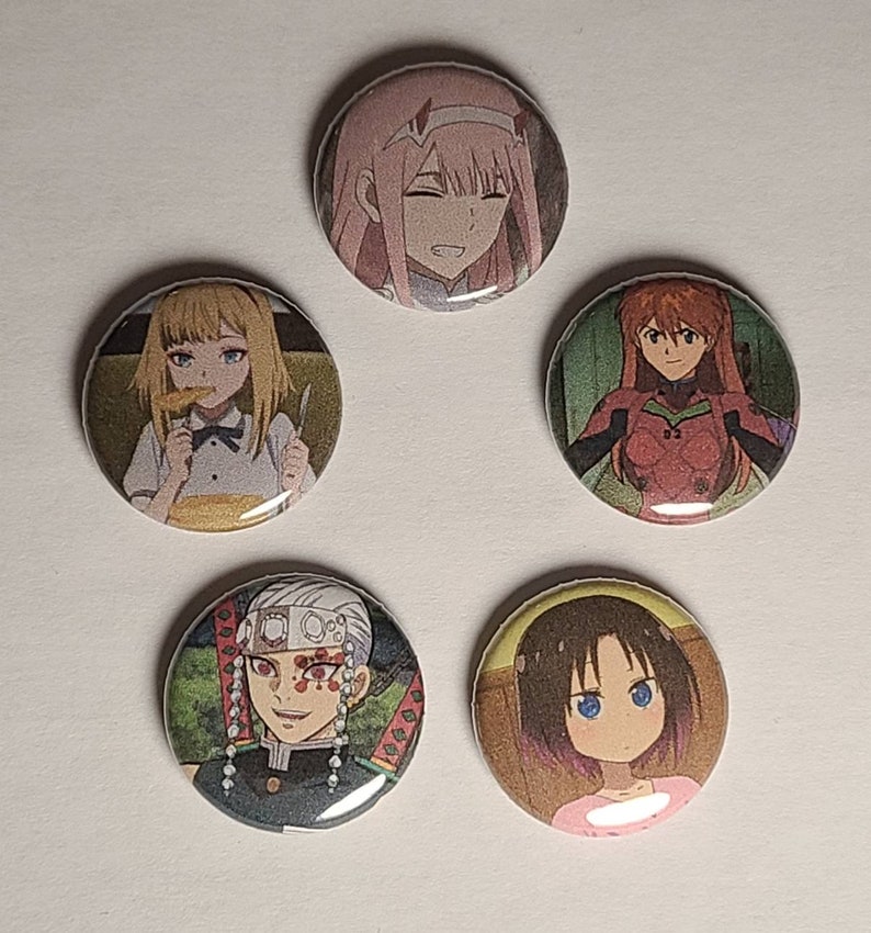 May include: Five round button pins featuring anime characters. The pins are colorful and feature various characters from different anime series.