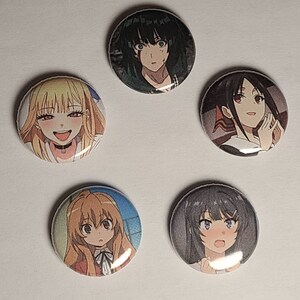 May include: Five round button pins featuring anime characters. The pins are colorful and feature different characters with various expressions.