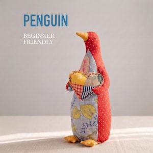 Puede incluir: Un peluche de pingüino hecho a mano con un cuerpo de lunares rojos, sosteniendo un corazón de retazos. El pingüino tiene un pico y pies amarillos, con una barriga con estampado floral azul. El texto superior dice "PENGUIN" y "BEGINNER FRIENDLY".