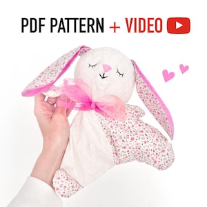 May include: A pink and white bunny plush toy with a pink bow and floral print fabric. The toy is being held by a hand. The image includes the text "PDF PATTERN + VIDEO"