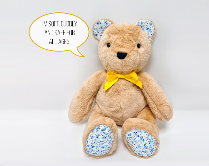 May include: A plush brown teddy bear with a yellow bow, blue and white floral ears and feet. The bear is sitting on a white surface. The text "I'm soft, cuddly, and safe for all ages!" is in a speech bubble above the bear.