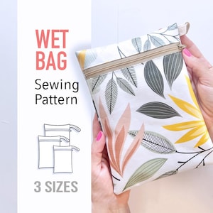 Puede incluir: Una bolsa impermeable blanca con un estampado floral colorido, sostenida por una persona. La bolsa tiene una cremallera beige y un lazo. El texto dice "WET BAG Sewing Pattern" y "3 SIZES".