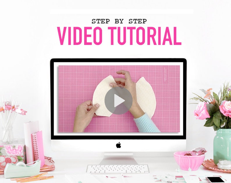 May include: A computer screen displaying a video tutorial on how to make a craft project. The video shows a person's hands holding a piece of white fabric on a pink cutting mat. The video is titled "Step by Step Video Tutorial".
