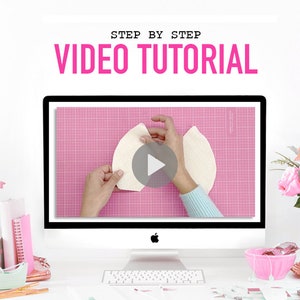 Pu&ograve; includere: Un monitor di computer che mostra un video tutorial passo dopo passo. Lo schermo mostra un paio di mani che lavorano con due pezzi di tessuto color bianco sporco e curvi su un tappetino da taglio rosa con griglia. Il monitor &egrave; su una scrivania.