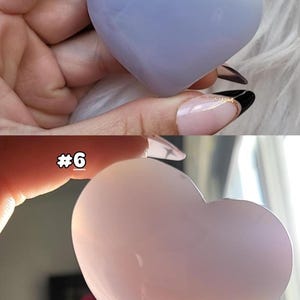 May include: Two heart-shaped stones, one light blue and the other pink, are displayed. The stones have a smooth, polished surface and are held in a person's hand. The top stone is a pale blue, while the bottom stone is a soft pink.