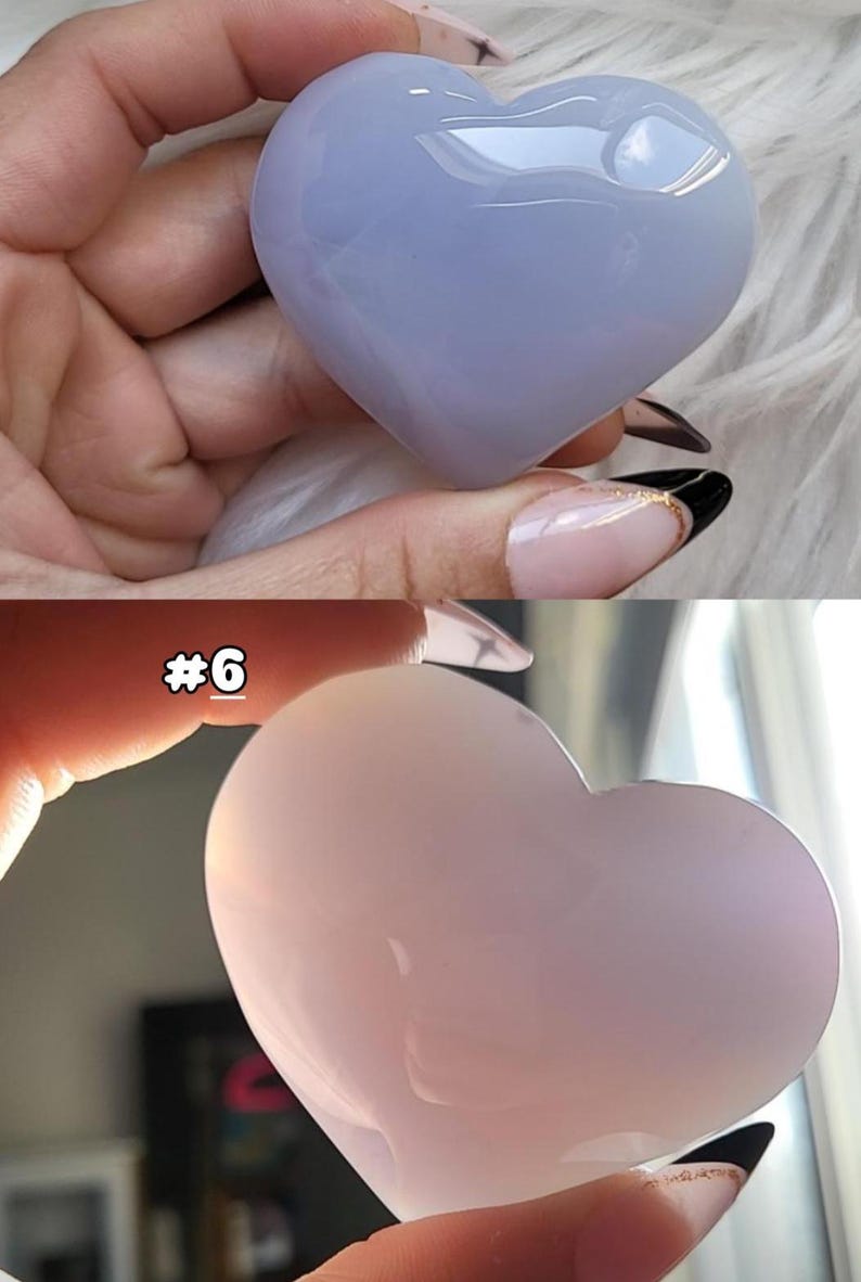 May include: Two heart-shaped stones, one light blue and the other pink, are displayed. The stones have a smooth, polished surface and are held in a person's hand. The top stone is a pale blue, while the bottom stone is a soft pink.