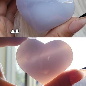 May include: Two heart-shaped stones, one light blue and the other pink, are held in a hand. The blue stone has a glossy finish, while the pink stone appears translucent. The number "#8" is visible in the image.