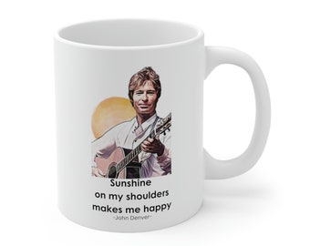May include: White ceramic mug with a color illustration of John Denver holding a guitar. The mug has the text "Sunshine on my shoulders makes me happy -John Denver- "