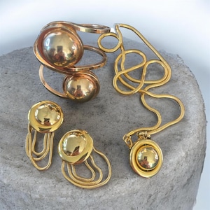 May include: A gold-toned jewelry set consisting of a cuff bracelet, a pair of dangle earrings, and a necklace. Each piece features a polished, spherical gold-toned accent. The earrings and necklace pendant include delicate gold-toned chain fringe.
