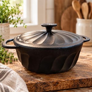 May include: A black cast iron Dutch oven featuring a fluted, scalloped design on both the body and the lid. The pot includes two side handles and a central knob on the lid, all finished in a matte black texture with a consistent radial pattern.