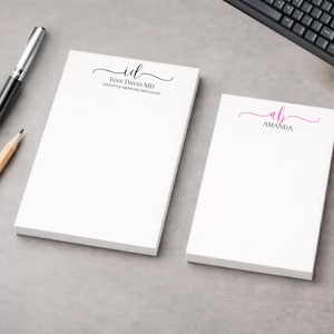 May include: Two white rectangular notepads with personalised text. The larger pad features the black text "id" with "IVAN DAVID MD LIFESTYLE MEDICINE SPECIALIST" below. The smaller pad features the pink text "ab" with "AMANDA" below.