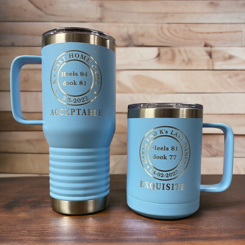 May include: Two blue stainless steel tumblers with gold lettering. The larger tumbler has the text "K's Last Home Game Heels 94 dook 81 3-5-2022 ACCEPTABLE". The smaller tumbler has the text "Heels End K's Last Dance Heels 81 dook 77 04-02-2022 EXQUISITE".