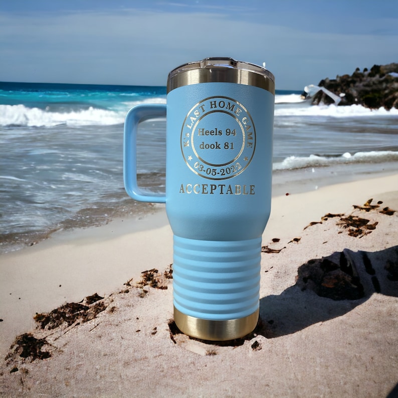 May include: A light blue stainless steel travel mug with a black handle. The mug has a gold lid and bottom. The mug has an engraved design that says "Last Home Game Heels 94 Dook 81 03-05-2023 Acceptable".