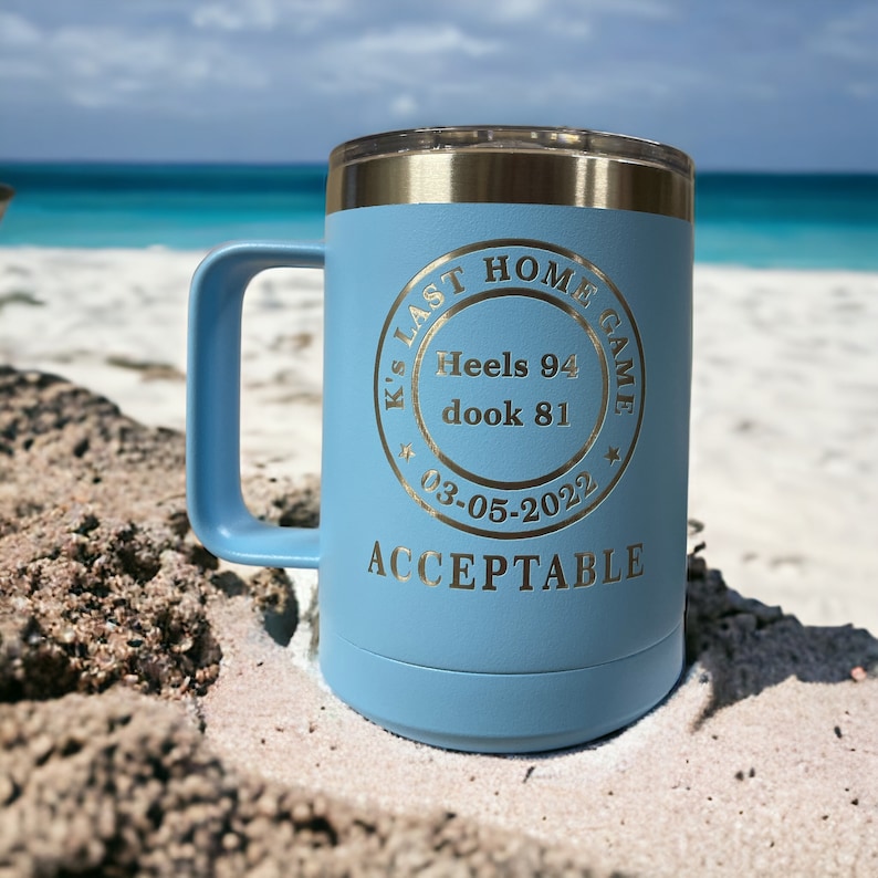 May include: A light blue travel mug with a gold inscription that reads "K's Last Home Game Heels 94 dook 81 03-05-2022 Acceptable".