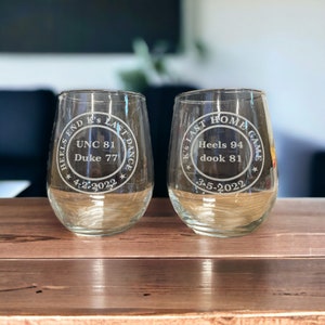 May include: Two clear glass wine glasses with etched designs commemorating the end of the basketball season. The first glass reads "HEELS END K's LAST DANCE UNC 81 Duke 77 * 4-2-2022 *" and the second glass reads "K's LAST HOME GAME Heels 94 dook 81 * 3-5-2022 *"