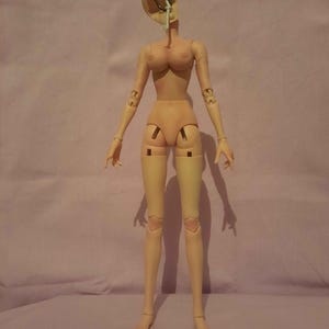May include: A nude-coloured articulated doll with a detached head and exposed internal mechanisms. The doll has a slender build, with visible joints at the shoulders, elbows, hips, and knees. The doll's head is open, revealing internal components.