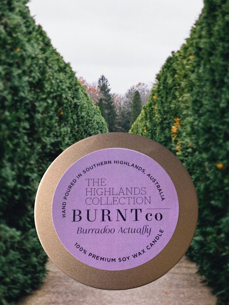 Puede incluir: Una lata de vela redonda, de color dorado, con una etiqueta morada. La etiqueta dice "The Highlands Collection BURNT co Burradoo Actually" y "100% Premium Soy Wax Candle". Tambi&eacute;n se ve el texto "Hand Poured in Southern Highlands, Australia".