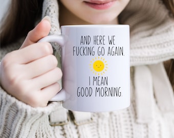 Pode incluir: Caneca de cerâmica branca com um design preto e amarelo. A caneca tem o texto "And here we fucking go again. I mean good morning."
