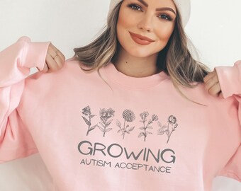 May include: Pink sweatshirt with a graphic of flowers and the text "Growing Autism Acceptance".