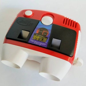 May include: Red and white plastic Batman and Robin View-Master with a black plastic frame and a clear plastic lens. The front of the viewer has a sticker with the text "The adventures of Batman and Robin".
