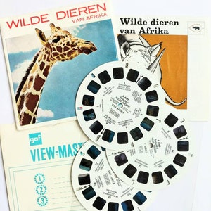 Puede incluir: Un conjunto de tres carretes View-Master con imágenes de animales salvajes de África. Los carretes son blancos con imágenes en negro y azul. El texto en los carretes dice "Wilde Dieren van Afrika".