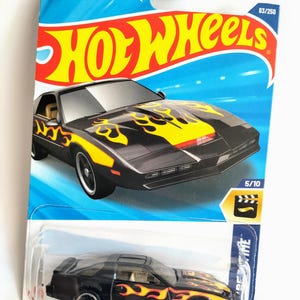 May include: A black Hot Wheels die-cast toy car of the Knight Rider vehicle. The car has yellow flames on the sides and a black and yellow stripe on the hood. The car is in a plastic blister pack with a blue background and the words "Knight Rider" and "Hot Wheels" on it. The car is number 83/250 and 5/10 in the series.