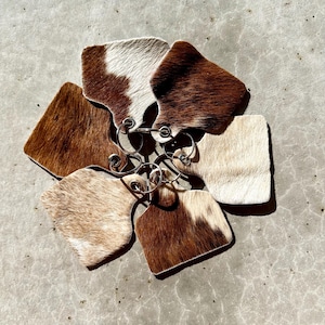 May include: A set of six cowhide keyrings with brown and white patterns. The keyrings are attached to a silver metal ring.