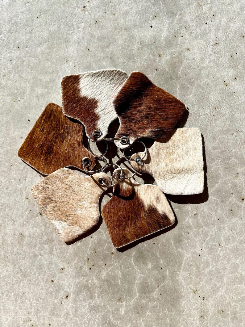 May include: A set of six cowhide keyrings with brown and white patterns. The keyrings are attached to a silver metal ring.