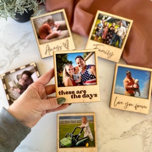 May include: Wooden photo frames with family photos. One frame reads "these are the days", another says "Love you forever", and another says "XOXO". The frames are held by a person.