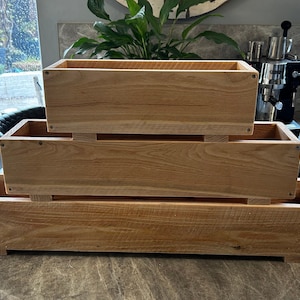 May include: Three wooden planter boxes stacked on top of each other. The boxes are made of natural wood and have a rustic look. The boxes are all the same size and shape, and they are all empty.