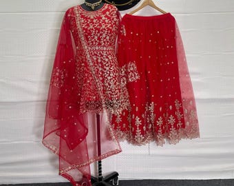 May include: A red embroidered formal outfit, including a top, pants, and a sheer scarf. The top and pants are adorned with gold embroidery. The outfit is displayed on a mannequin with a black stand. A circular sign with gold lettering is visible.