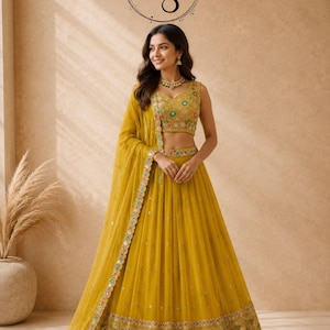 May include: A mustard yellow lehenga choli set featuring a sleeveless blouse and a floor-length skirt with intricate multi-colored floral embroidery, mirror work, and a matching sheer dupatta with a decorative border, marked with the AAYNA STORE logo.