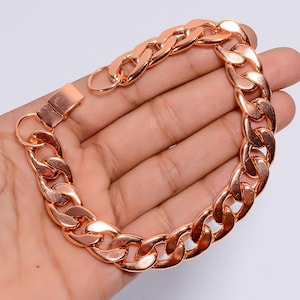 Può includere: Un bracciale a catena a maglia a catena in oro rosa con una chiusura sicura. Il bracciale presenta grandi maglie ad incastro, creando un accessorio audace ed elegante. La calda tonalità metallica del bracciale suggerisce un gioiello classico e versatile.