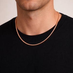 以下が含まれることがあります： 織り模様のローズゴールドチェーンネックレス。 ネックレスは黒い背景に表示され、金属の暖かい色合いが強調されています。 チェーンは繊細なアクセサリーです。