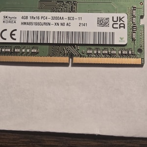 Könnte beinhalten: Ein grüner und goldener RAM-Riegel mit dem Text "SK hynix 4GB 1Rx16 PC4-3200AA-SCO-11" und anderen technischen Spezifikationen. Der Riegel hat eine Reihe goldener Anschlüsse entlang der Unterkante und einen Barcode.