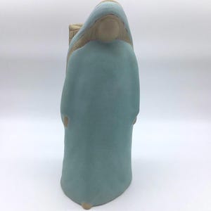 May include: A ceramic figurine of a person wearing a light blue robe. The figurine is standing with its hands clasped in front of it.