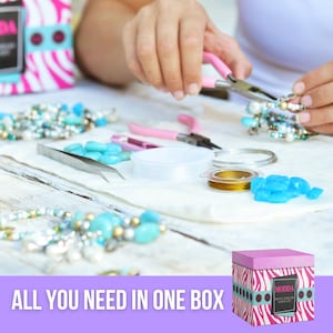 Pu&ograve; includere: Una scatola con motivo zebrato rosa e bianco con il testo "MODDA JEWELRY MAKING KIT" sul davanti. La scatola &egrave; aperta e contiene vari materiali per la creazione di gioielli, tra cui perline, filo, corda e pinze. Il testo "ALL YOU NEED IN ONE BOX" &egrave; visualizzato su uno sfondo viola.