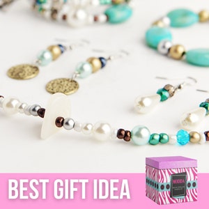 Pu&ograve; includere: Un kit per la creazione di gioielli in una scatola a stampa zebra rosa e bianca. La scatola ha il testo "MODDA Creative Jewelry Making Kit" sul davanti. Il kit include una collana, orecchini e perline di vari colori, tra cui bianco, blu, verde e marrone.