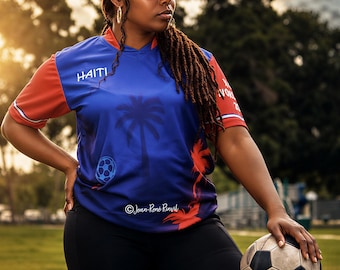 May include: A blue and red Haiti soccer jersey with a palm tree and soccer ball graphic, the text HAITI, and a matching visor featuring the Haitian flag. The jersey is paired with black leggings and a worn black and white soccer ball.