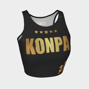 Puede incluir: Top corto negro con texto dorado brillante "KONPA" y cinco estrellas doradas. El top tiene un diseño de espalda deportiva y un escote redondo. La palabra "KONPA" está en negrita, fuente sans-serif.