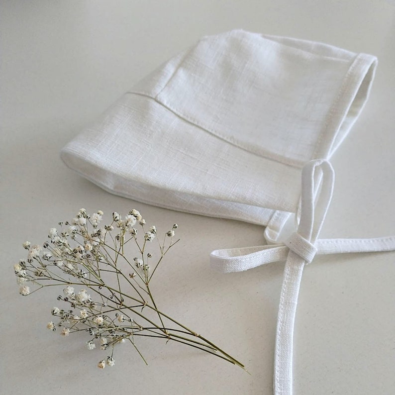 Puede incluir: Un gorro blanco de lino con un lazo atado. El gorro est&aacute; hecho de una tela suave y ligera y tiene un dise&ntilde;o simple y elegante.
