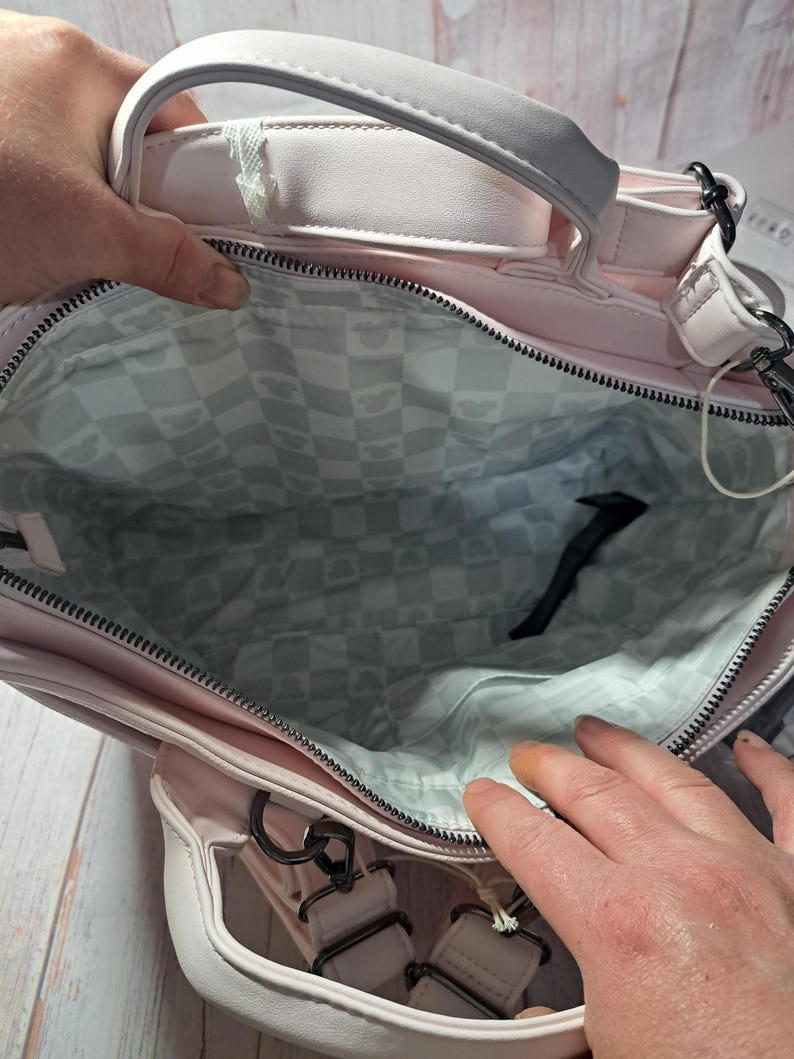 May include: A light pink handbag with a top handle and a detachable shoulder strap. The interior lining features a checkered pattern with a repeating design. The bag has a zipper closure and metal hardware.