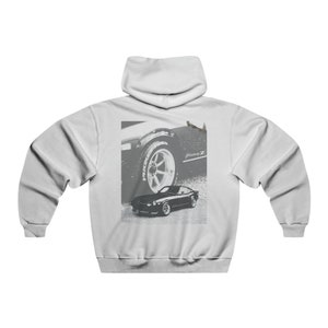 Puede incluir: Una sudadera con capucha blanca con una imagen en blanco y negro de un coche clásico en la parte posterior. El coche es un Datsun 240Z con el texto "Fairlady Z" en el lateral.