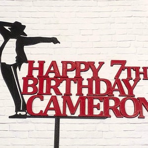 May include: Red and black cake topper featuring a silhouette of Michael Jackson with the text "Happy 7th Birthday Cameron".